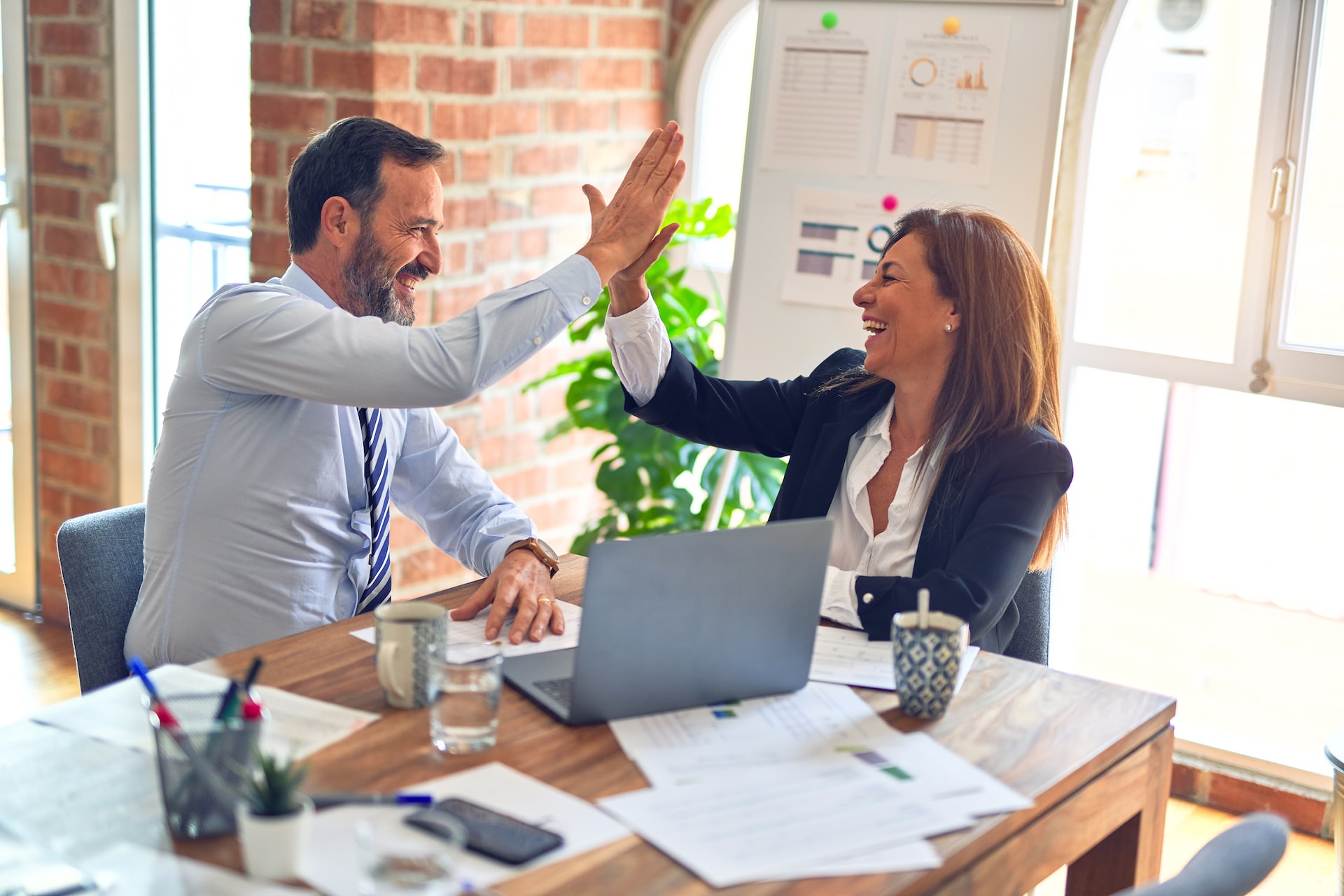 A picture of a man and a woman high fiving while sat at a desk with business papers